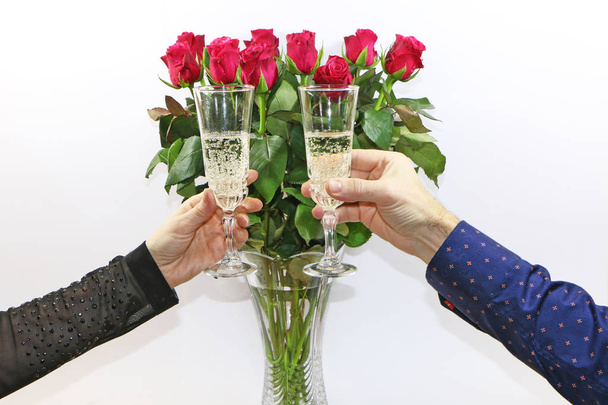 close up - man and woman holding glasses of champagne on a background of red roses - Fotó, kép