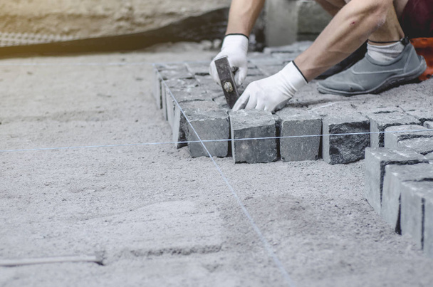 Worker lays gray granite pavement tiles on marked site. Arrangement of urban environment. Repair of city roads - Фото, зображення