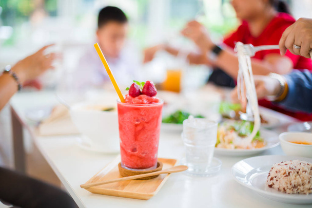 Suco Batido de morango na mesa branca no restaurante com mulheres embaçadas e crianças estão comendo alimentos
 - Foto, Imagem