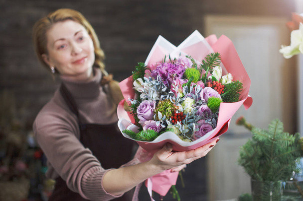 Девушка-флористка в коричневом фартуке показывает покупателю красивый букет в цветочном салоне на праздничный подарок на свадьбу или юбилей
. - Фото, изображение
