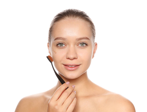 Young woman applying foundation on her face against white background - Foto, Imagen