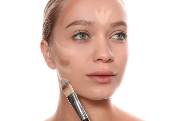Young woman applying foundation on her face against white background - Foto, Imagem