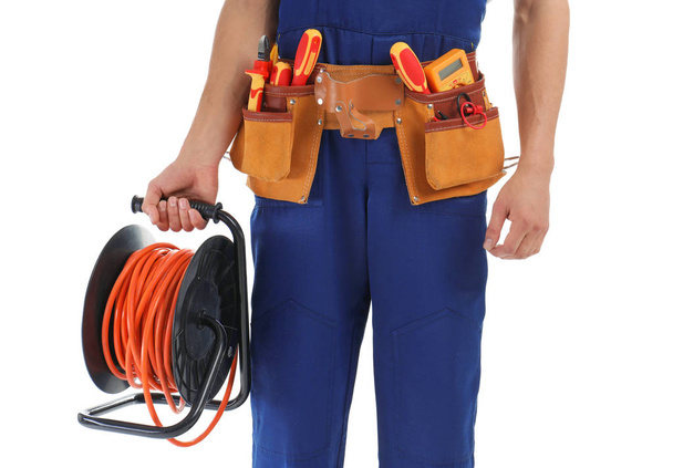 Electrician with extension cord reel and tools wearing uniform on white background, closeup - Fotoğraf, Görsel