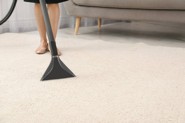 Woman removing dirt from carpet with vacuum cleaner indoors, closeup. Space for text - Photo, Image