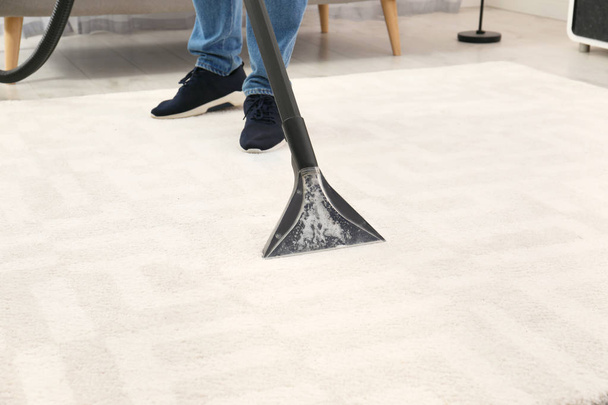 Man removing dirt from carpet with vacuum cleaner indoors, closeup - Fotó, kép