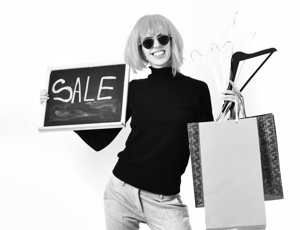 girl in wig holding package, hangers, board with sale inscription - 写真・画像