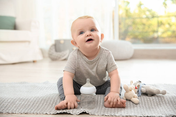 Cute baby with bottle sitting on floor in room - Foto, Bild