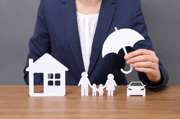 Woman with cutout paper family, house, car and umbrella at table, closeup. Life insurance concept - Photo, Image