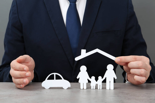 Man with cutout paper family, house roof and car at table, closeup. Life insurance concept - Foto, Bild