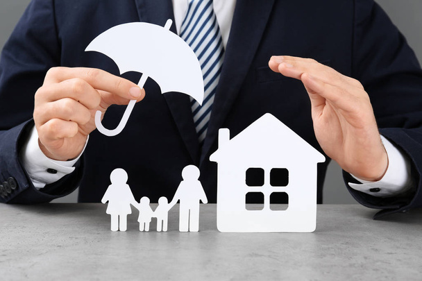 Man with cutout paper family, house and umbrella at table, closeup. Life insurance concept - Photo, Image