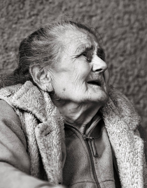 Old age and lifestyle concept. Black and white portrait of a very old and tired wrinkled woman outdoors. Very old hoary woman face closeup portrait. Aging process - very old senior women - Photo, Image