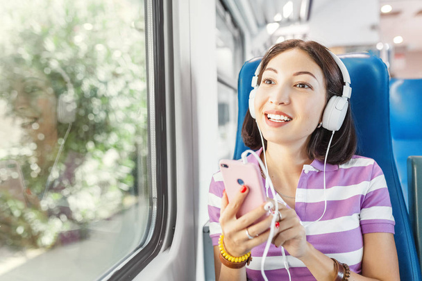 Genç bir Asyalı kadın bir müzik dinliyor veya podcast ve bir tren seyahat ederken onun smartphone kablosuz internet kullanarak sohbet - Fotoğraf, Görsel