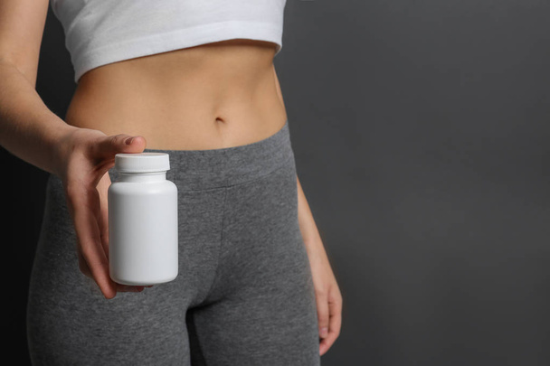 Slim woman holding bottle of weight loss pills against gray background, closeup. Space for text - Fotoğraf, Görsel