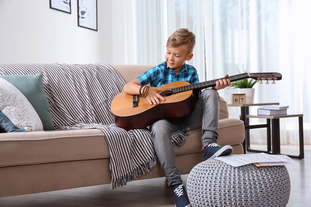 Cute little boy playing guitar on sofa in room - Valokuva, kuva