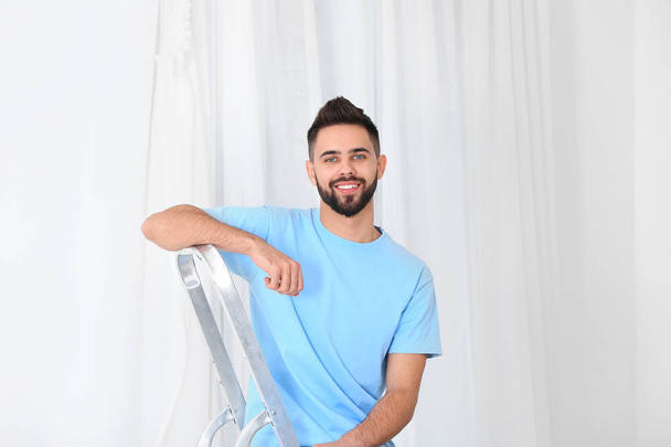 Young man sitting on stepladder near window with curtain in room - Foto, Imagem