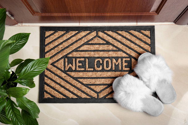 Welcome doormat and white slippers at door in hall, top view - Zdjęcie, obraz
