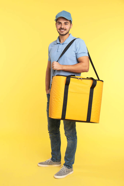 Young courier with thermo bag on color background. Food delivery service - Foto, afbeelding