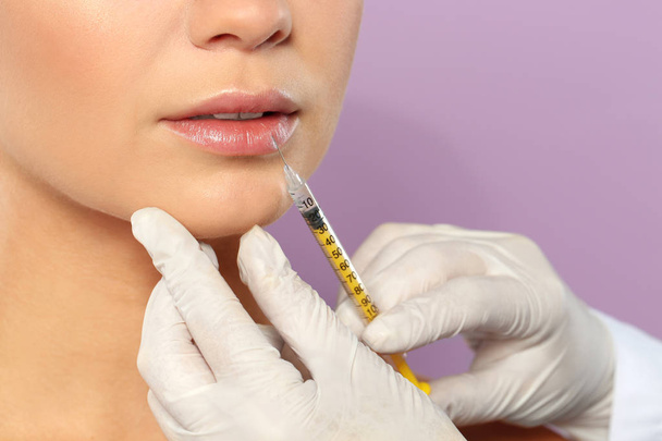 Mujer joven recibiendo la inyección de labios en el fondo de color, primer plano. Cirugía estética
 - Foto, imagen