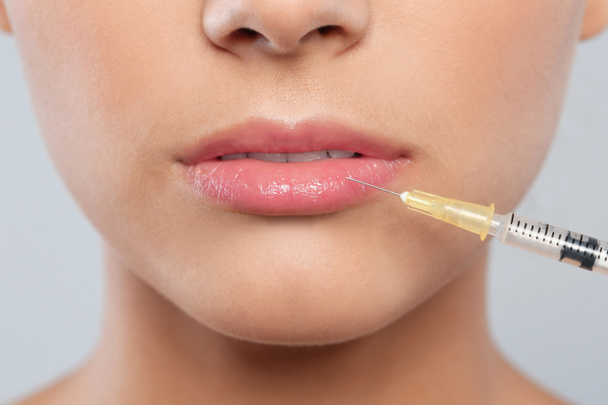Jonge vrouw krijgen lippen injectie op grijze achtergrond, close-up. Cosmetische chirurgie - Foto, afbeelding