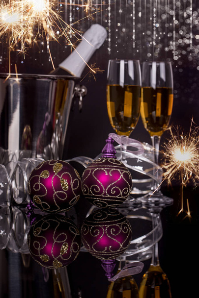 Two wine glasses with champagne, bottle in bucket, sparklers and Christmas ornaments on a black background. Copy space. Merry Christmas and Happy New Year, background - Photo, Image