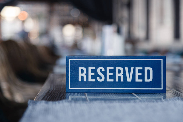 Closeup ξύλινα μπλε λευκό ορθογώνιο πιάτο με το στέκεται δεσμευμένη λέξη σε γκρι τραπέζι στο εστιατόριο. Έννοια της προετοιμασίας για το Συμπόσιο, κλειστό μπουφέ στο γάμο, μπάτσελορ πάρτι - Φωτογραφία, εικόνα