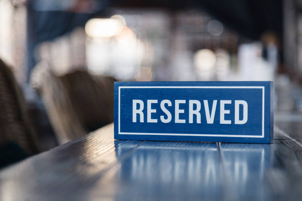 Closeup de madeira azul placa retangular branco com a palavra Reservado de pé sobre mesa cinza no restaurante. Conceito de preparação para o banquete, buffet fechado no casamento, despedida de solteiro
 - Foto, Imagem