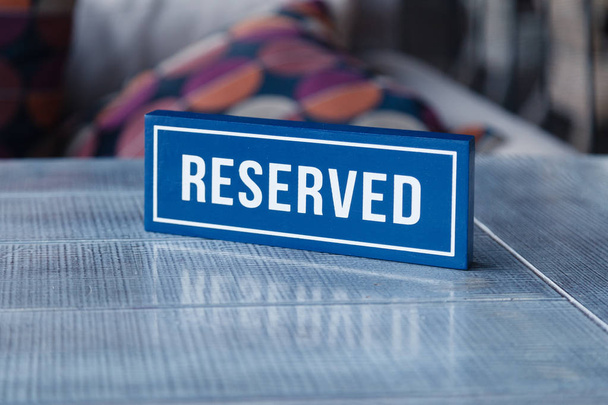 Closeup wooden blue white rectangular plate with the word Reserved standing on gray table in restaurant. Concept of preparation for banquet, closed presentation, buffet, degustation wine - Photo, Image