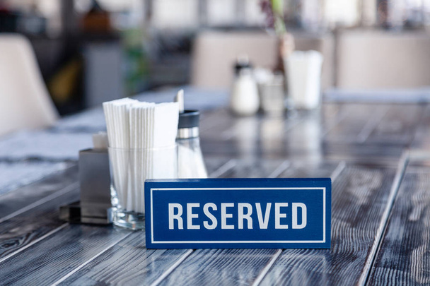 Closeup wooden blue white rectangular plate with word Reserved standing on gray vintage table in restaurant near to the serving, white paper napkins, salt and pepper shaker, sugar bowl - Photo, Image