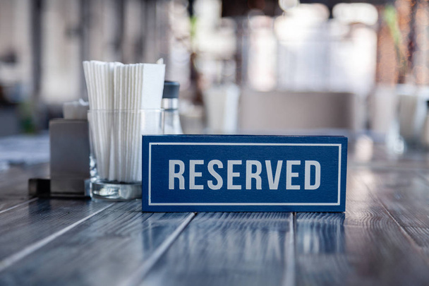 Placa rectangular azul de madera con palabra Reservado de pie sobre mesa vintage gris en restaurante cerca de la porción, servilletas de papel blanco, salero y pimentero, tazón de azúcar
 - Foto, Imagen