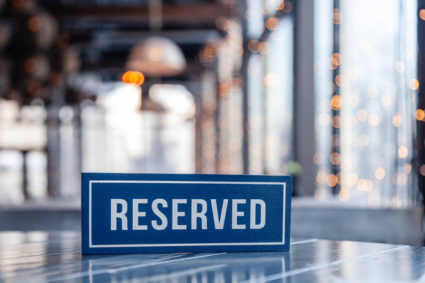 Closeup wooden blue white rectangular plate with the word Reserved standing on gray table in restaurant. Concept of preparation for the banquet, closed buffet at the wedding, bachelor party - Photo, Image