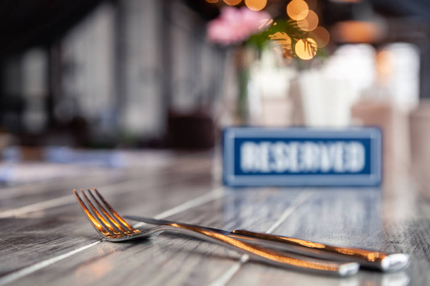 Closeup μετάλλων πιρούνι και μαχαίρι κοντά σε ξύλινα μπλε λευκό ορθογώνιο πιάτο με το στέκεται δεσμευμένη λέξη σε γκρι vintage τραπέζι στο εστιατόριο. Μαλακή εστίαση, θολή αντικείμενο. Έννοια κλειστό δεξιώσεων - Φωτογραφία, εικόνα