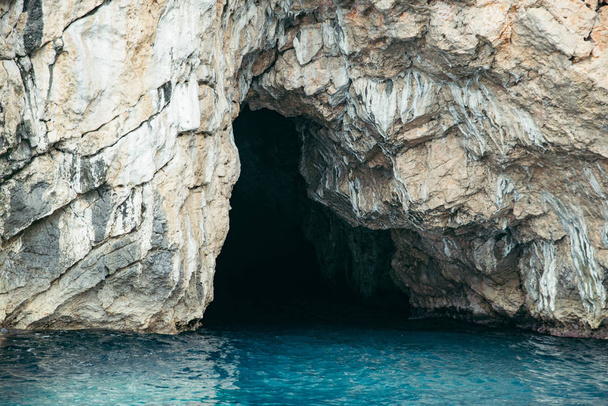 view of grotto in rocky cliff with azure water. summer vacation concept - Photo, Image