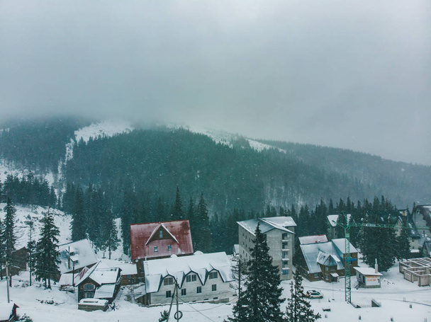 Widok z lotu ptaka o małej wiosce w górach zasypani. pochmurny pogody. Burza śnieżna - Zdjęcie, obraz