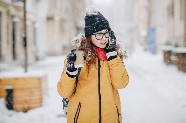 Girl drinking coffee and talking on the phone outside in winter - 写真・画像