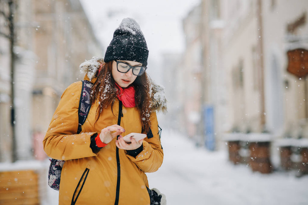 Portrait of beautiful happy young woman with smartphone over christmas lights in winter - Photo, Image