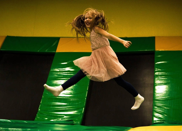 Little girl is jumping on a trampoline in kids play room on her birthday - Фото, зображення