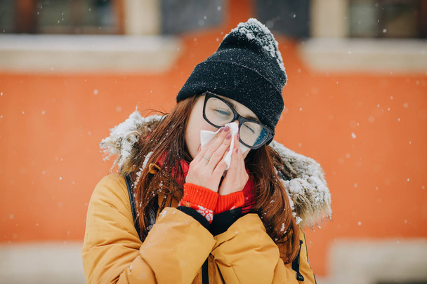 Young woman blowing her nose into a tissue in winter - Foto, afbeelding
