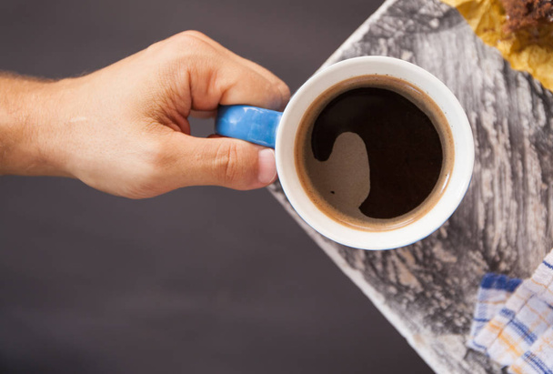 Cup of black coffeein male hand on the background of the wooden surface at the corner of the table. Flat layout - Photo, Image