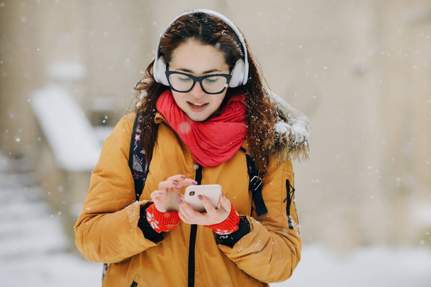 Woman listen to music on mobile phone in the city at winter time. Portrait close-up young woman in the winter city, smiling - Photo, image