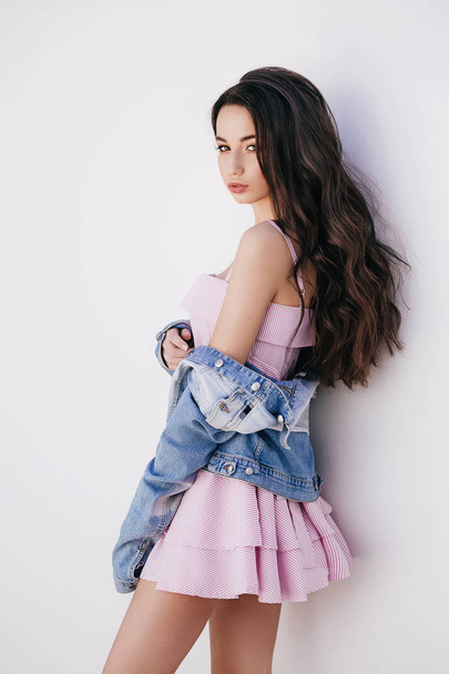 Portrait of beautiful young   posing in pink dress and jeans jacket - Фото, зображення