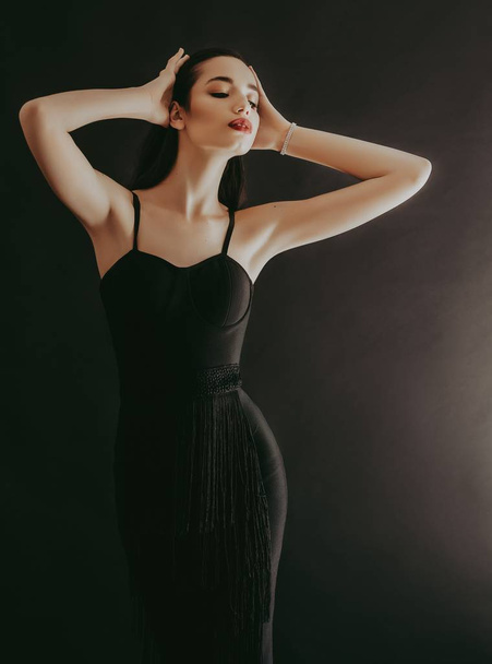 Bella giovane donna in posa in abito nero in studio
 - Foto, immagini