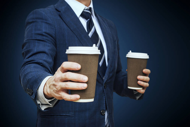 Businessman offering coffee in paper cup. Businessman offers a cup of coffee. Businessman holding two disposable coffee cup - Foto, imagen