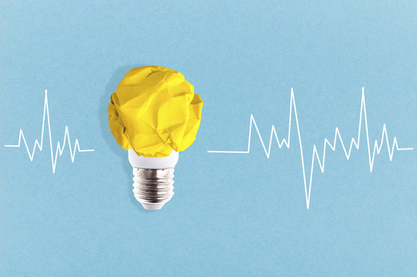 bulbo de luz de papel amarillo arrugado cerca de un cardiograma sobre un fondo azul, idea conceptual
 - Foto, imagen