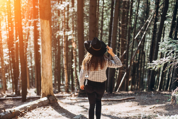 Woman in hat walking in at amazing coniferous forest an in sunset time.  Concept adventure active vacations outdoor, space for text, atmospheric epic moment  - Foto, imagen