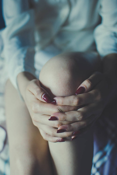 Skinny pale young girl wearing a white shirt and shorts sitting and holding her hands together on her knees - Fotoğraf, Görsel