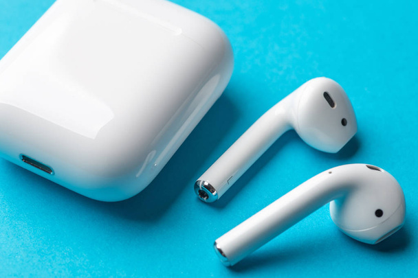 Άσπρο ασύρματο bluetooth ακουστικά ή ακουστικά και λευκό κουτί για την αποθήκευση και φόρτιση σε μπλε φόντο - Φωτογραφία, εικόνα