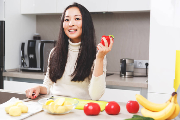 Foto de mujer joven con pimienta en la mano de pie a la mesa con verduras y frutas
 - Foto, Imagen