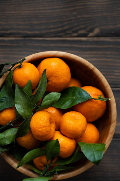 Tangerines - oranges, mandarins, clementines, citrus fruits, with leaves in basket over wooden background - Photo, Image