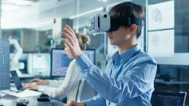 Computer Science Engineer wearing Virtual Reality Headset Works with 3D Modeling, Makes Gestures. In the Background Engineering Bureau with Busy Coworkers. - Metraje, vídeo