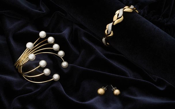 Gouden armbanden en oorbellen paar op blauwe fluwelen stof achtergrond - Foto, afbeelding